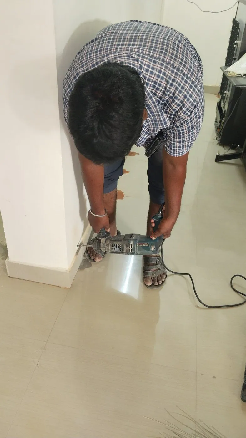 Technician drilling the floor next to a wall for termite drill-and-inject treatment